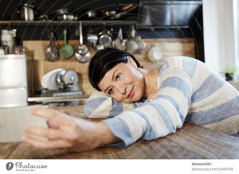 Frau in Küche ruht sich auf Tisch aus und hält Handy lächeln Selfie Selfies Mobiltelefon Handies Handys Mobiltelefone weiblich Frauen Telefon telefonieren