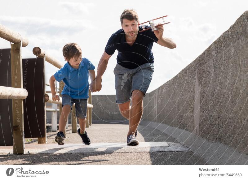 Vater und Sohn rennen mit Spielzeugflugzeug Papas Väter Vati Vatis Papis glücklich Glück glücklich sein glücklichsein Flugzeug Flieger Flugzeuge spielen Söhne