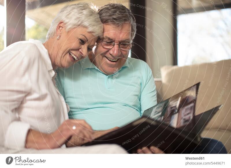 Glückliches älteres Paar sitzt auf der Couch und schaut sich ein Fotoalbum an Sofa Couches Liege Sofas sitzen sitzend ansehen glücklich glücklich sein