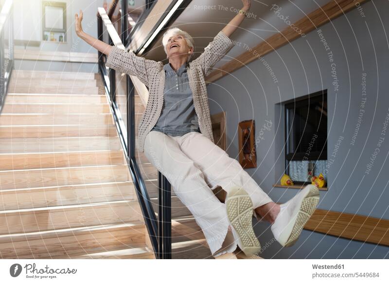 Glückliche ältere Frau rutscht eine Treppe hinunter Seniorin Seniorinnen alt Geländer rutschen Altersheim Altenheim Seniorenheim Treppenaufgang lachen weiblich