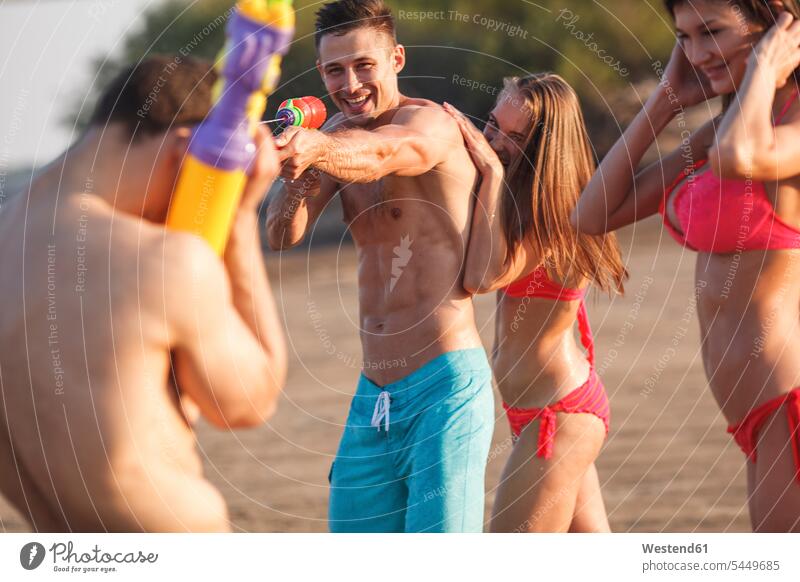 Glückliche Freunde spielen mit Wasserpistolen am Strand Spaß Spass Späße spassig Spässe spaßig Beach Straende Strände Beaches Freundschaft Kameradschaft
