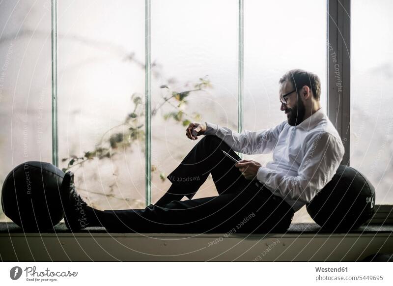 Geschäftsmann sitzt auf dem Fensterbrett und liest Textnachrichten Fensterbank Fenstersims Fensterbänke Smartphone iPhone Smartphones Businessmann