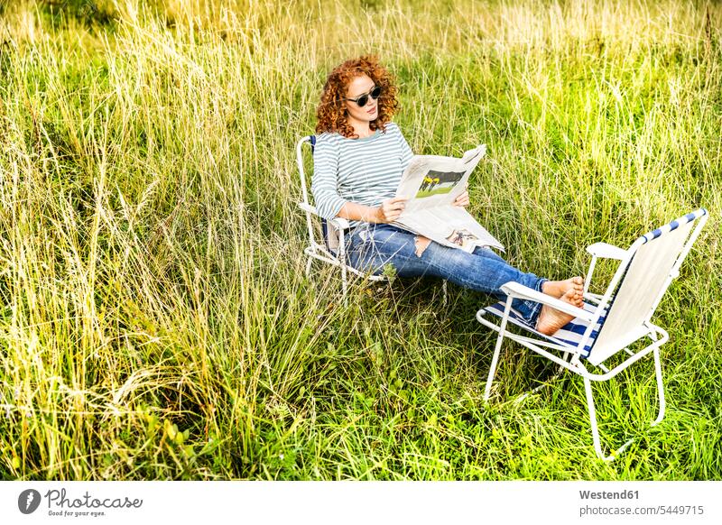 Junge Frau entspannt sich auf einer Wiese und liest Zeitung Zeitungen weiblich Frauen lesen Lektüre Erwachsener erwachsen Mensch Menschen Leute People Personen