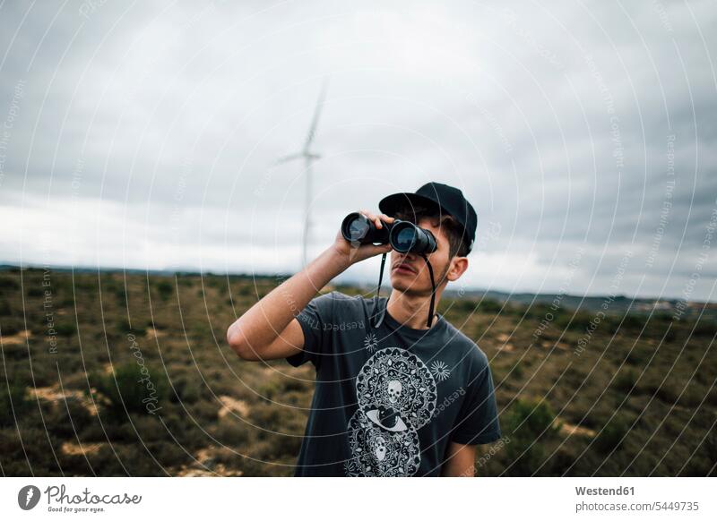 Spanien, Lleida, junger Mann schaut durch ein Fernglas in eine ländliche Landschaft Männer männlich Ferngläser Feldstecher Fernglaeser schauen schauend