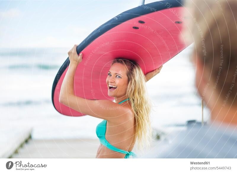 Glückliche Frau mit Surfbrett tragen transportieren Strand Beach Straende Strände Beaches Surfen Surfing Wellenreiten lachen gehen gehend geht Surfbretter