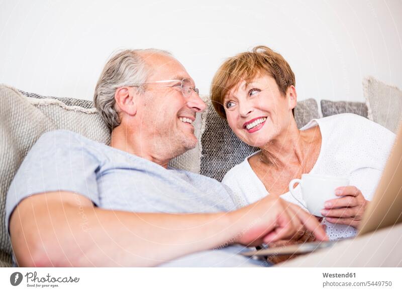 Glückliches älteres Ehepaar zu Hause, das mit einem Laptop auf der Couch sitzt Sofa Couches Liege Sofas Notebook Laptops Notebooks lächeln entspannt