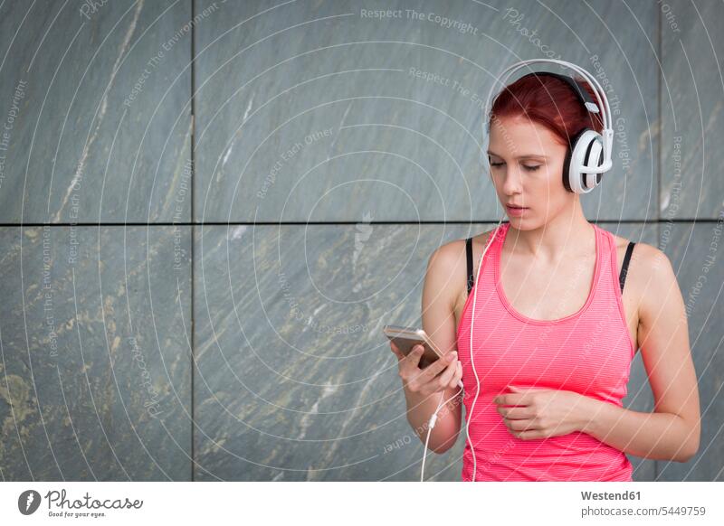 Frau in Sportkleidung mit Kopfhörern, die Musik hört weiblich Frauen Workout fit Smartphone iPhone Smartphones trainieren jung Erwachsener erwachsen Mensch