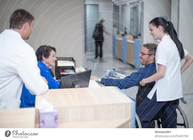 Patienten im Rollstuhl im Gespräch mit dem Personal an der Rezeption Rollstühle Rollstuehle Rolli Rollis Krankenhaus Kliniken Krankenhäuser Krankenhaeuser