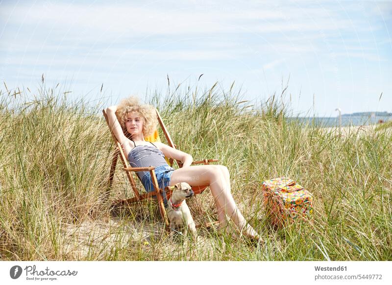 Porträt einer jungen Frau, die im Strandkorb in den Dünen sitzt und etwas beobachtet Wiese Wiesen Liegestuhl Strandstuhl weiblich Frauen Erwachsener erwachsen