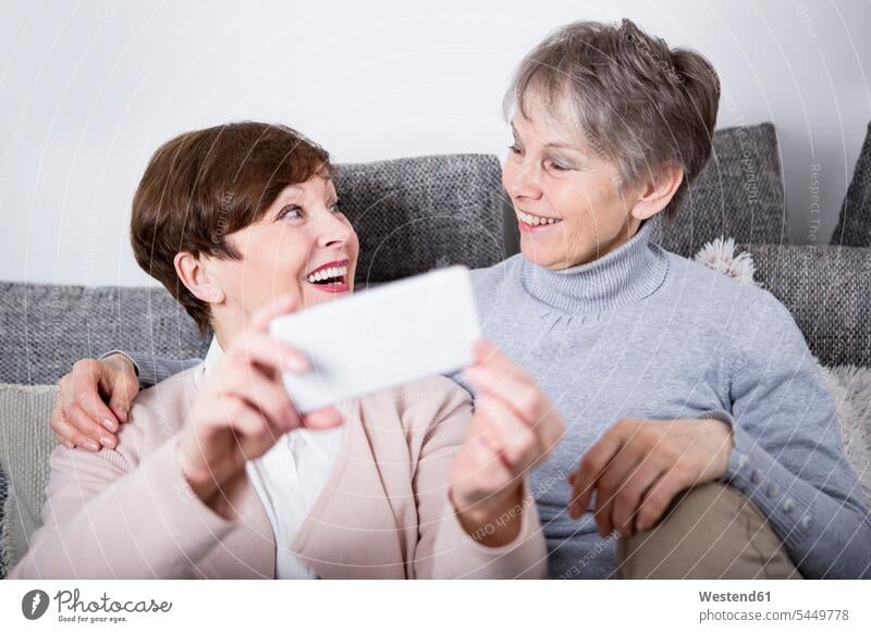 Zwei ältere Frauen sitzen auf einer Couch, Freundinnen Gemeinsam Zusammen Miteinander Selfie Selfies Seniorin Seniorinnen alt sitzend sitzt fotografieren Handy