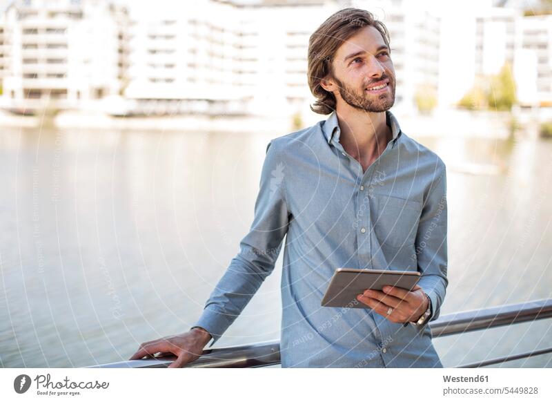 Junger Mann steht am Geländer und hält digitales Tablett stehen stehend Mobilität mobil unterwegs auf Achse in Bewegung denken nachdenken Tablet Computer