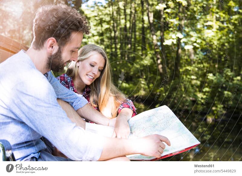 Lächelndes junges Paar beim Kartenlesen an einem Bach Bäche Baeche Pärchen Paare Partnerschaft Wald Forst Wälder lächeln ansehen Landkarte Landkarten Gewässer