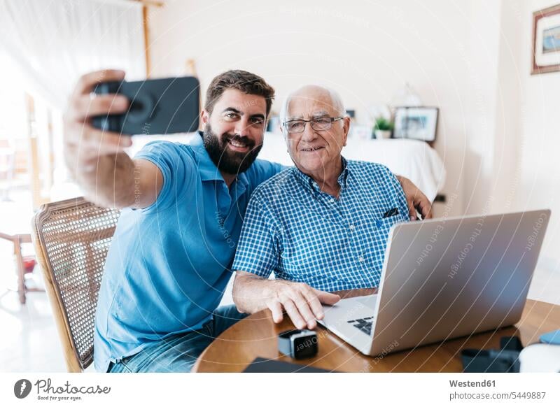 Porträt eines erwachsenen Enkels und seines Großvaters, die zu Hause ein Selfie mit dem Smartphone machen Enkelsöhne Enkelsohn Portrait Porträts Portraits Opa