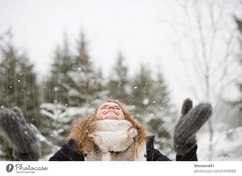 Glückliche junge Frau geniesst Schneefall im Winterwald weiblich Frauen Erwachsener erwachsen Mensch Menschen Leute People Personen schneien Bewunderung