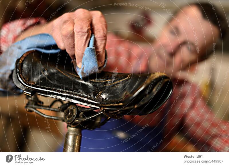 Älterer Mann reinigt Fahrradsitz in seiner Werkstatt, Nahaufnahme Senior ältere Männer älterer Mann Senioren Hand Hände Fahrradsattel Sattel Sättel Fahrradsitze