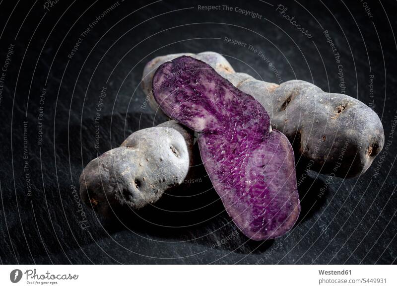 Ganze und in Scheiben geschnittene violette Kartoffeln auf Schiefer ungekocht roh rohe Kartoffeln Schieferstein Schiefersteine Hälfte halbe halbiert halber