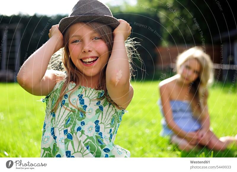 Fröhlich verspieltes Mädchen setzt im Garten einen Hut auf Spaß Spass Späße spassig Spässe spaßig lachen Gärten Gaerten weiblich Hüte positiv Emotion Gefühl