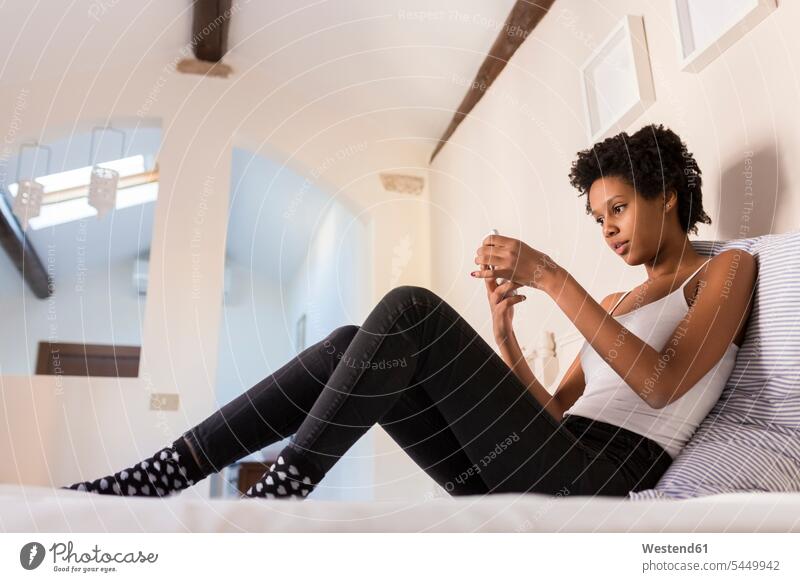 Junge Frau benutzt Mobiltelefon im Schlafzimmer weiblich Frauen Zuhause zu Hause daheim Handy Handies Handys Mobiltelefone Bett Betten Zimmer Raum Räume