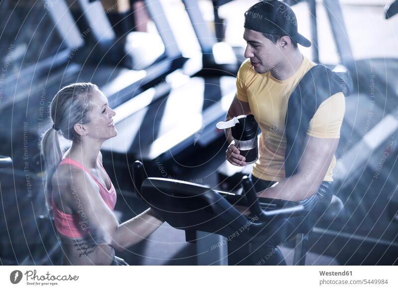 Junger Mann und Frau unterhalten sich im Fitnessstudio Fitnessclubs Fitnessstudios Turnhalle Heimtrainer Hometrainer Trimmräder Trimmrad lächeln trainieren fit