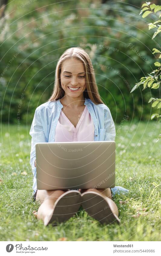 Lächelnde junge Frau mit Laptop auf einer Wiese lächeln Park Parkanlagen Parks weiblich Frauen Notebook Laptops Notebooks Erwachsener erwachsen Mensch Menschen
