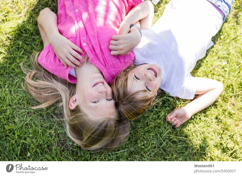 Zwei glückliche Schwestern liegen auf der Wiese liegend liegt Glück glücklich sein glücklichsein entspannt entspanntheit relaxt Wiesen Garten Gärten Gaerten