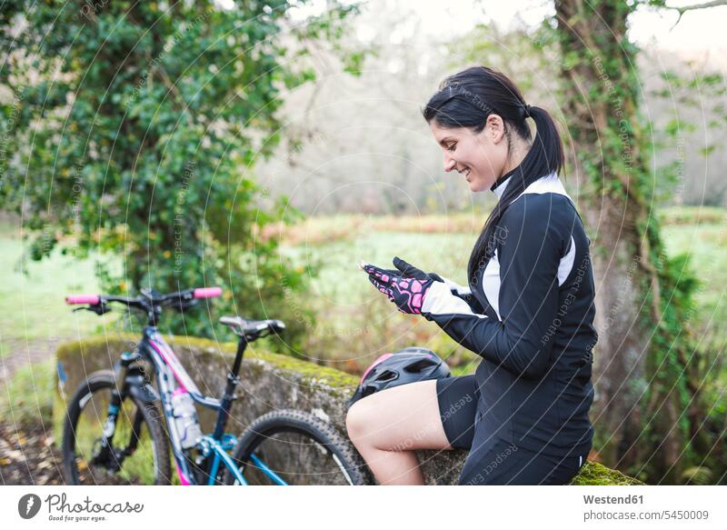 Glückliche Frau mit Mountainbike, die ihr Handy überprüft weiblich Frauen Mountainbiking mountainbiken MTB Mobiltelefon Handies Handys Mobiltelefone