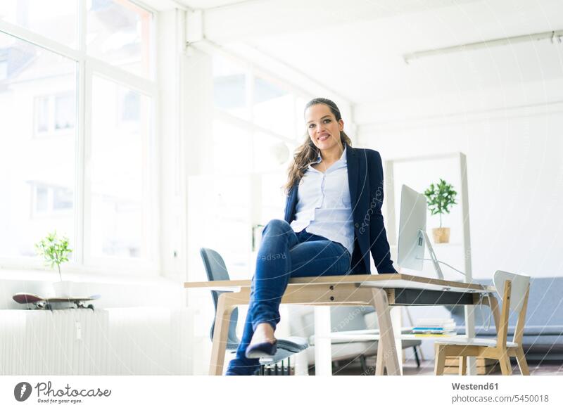 Porträt einer lächelnden Geschäftsfrau, die auf einem Tisch in einem Loft sitzt sitzen sitzend Geschäftsfrauen Businesswomen Businessfrauen Businesswoman Frau