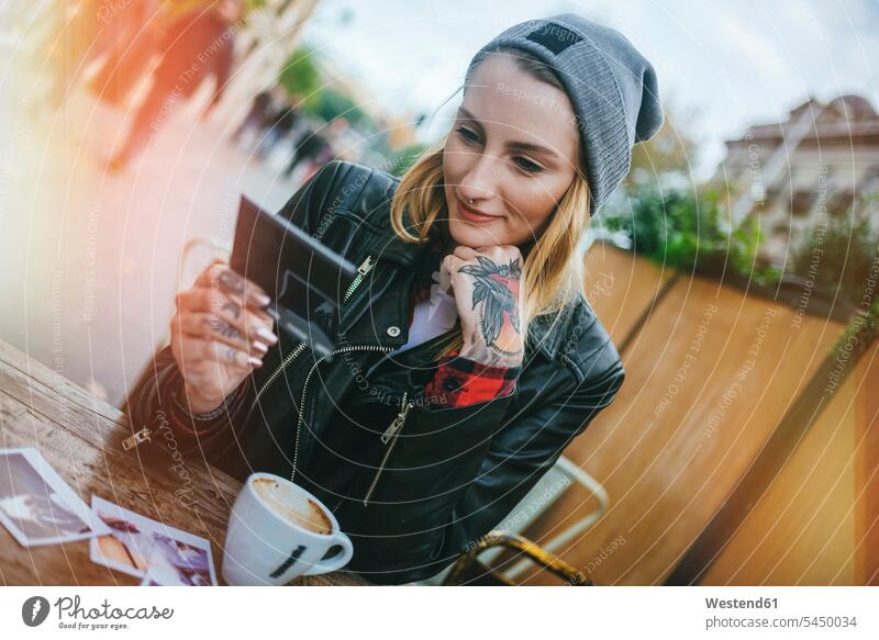 Junge tätowierte Frau sitzt in einem Straßencafé und schaut sich Fotos an weiblich Frauen Straßencafe Straßencafes Strassencafe Strassencafes Portrait Porträts