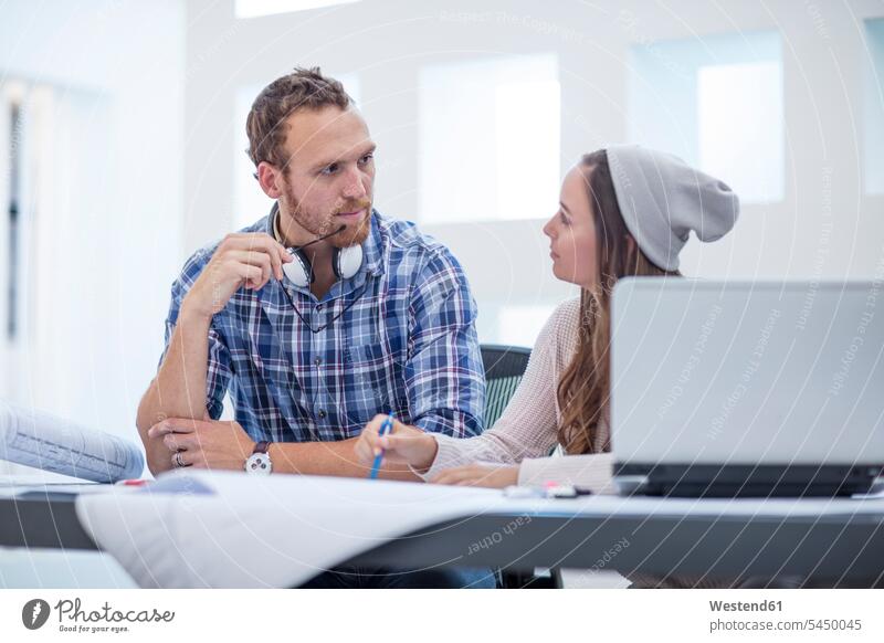 Junger Mann und Frau diskutieren Projekt im Designbüro Büro Office Büros Laptop Notebook Laptops Notebooks Gemeinsam Zusammen Miteinander arbeiten Arbeit