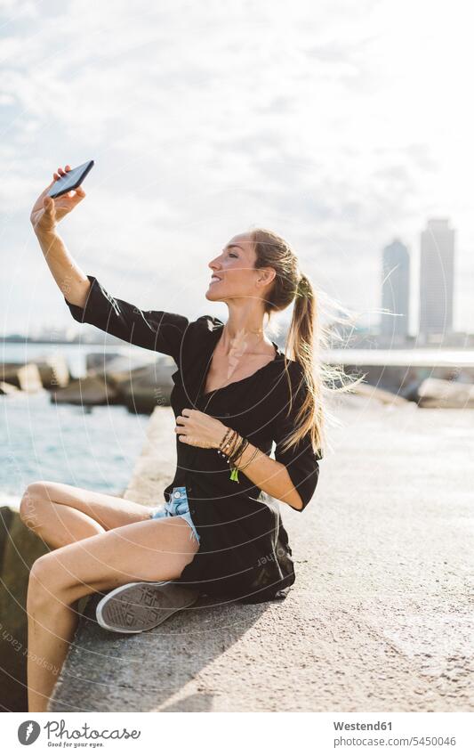 Junge Frau macht ein Selfie an der Strandpromenade Selfies weiblich Frauen lächeln Handy Mobiltelefon Handies Handys Mobiltelefone glücklich Glück