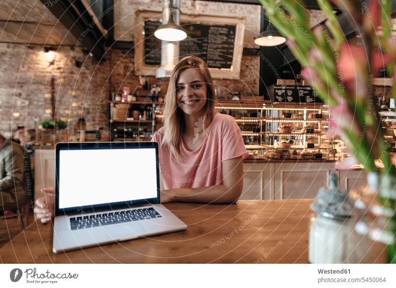 Junge Frau sitzt im Café, mit Laptop auf dem Tisch Notebook Laptops Notebooks lächeln sitzen sitzend Cafe Kaffeehaus Bistro Cafes Cafés Kaffeehäuser glücklich