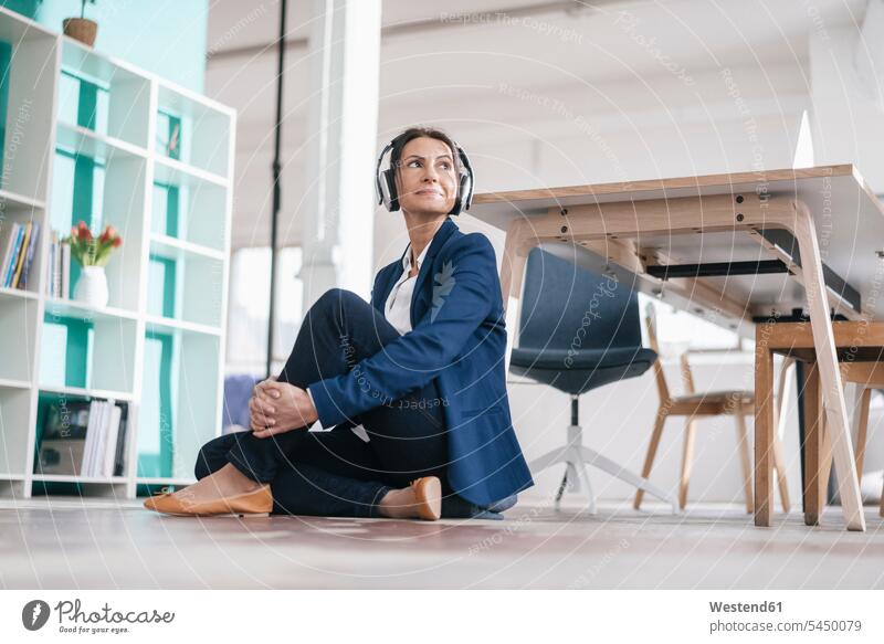 Geschäftsfrau, die in einem Loft auf dem Boden sitzt und mit Kopfhörern Musik hört Kopfhoerer Geschäftsfrauen Businesswomen Businessfrauen Businesswoman Frau