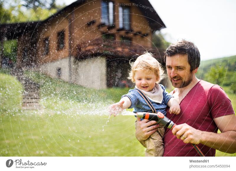 Kleiner Junge mit seinem Vater beim Bewässern des Rasens Sohn Söhne Schlauch Schläuche Schlaeuche Garten Gärten Gaerten Papas Väter Vati Vatis Papis Kind Kinder