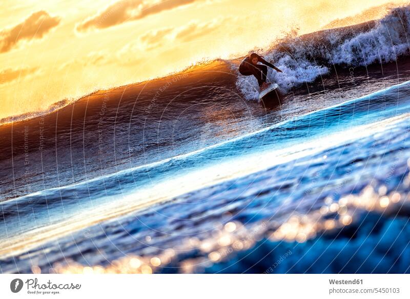 Junge Frau surft bei Sonnenuntergang im Meer Surferin Wellenreiterinnen Surferinnen Surfen Surfing Wellenreiten Wassersport Sport wellenreiten weiblich Frauen