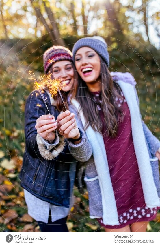 Zwei glückliche Frauen halten Wunderkerzen in einem herbstlichen Wald Freundinnen Glück glücklich sein glücklichsein Forst Wälder weiblich schön Herbst Freunde