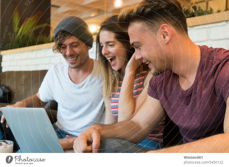 Drei aufgeregte Freunde schauen sich in einem Café einen Laptop an Notebook Laptops Notebooks glücklich Glück glücklich sein glücklichsein Cafe Kaffeehaus