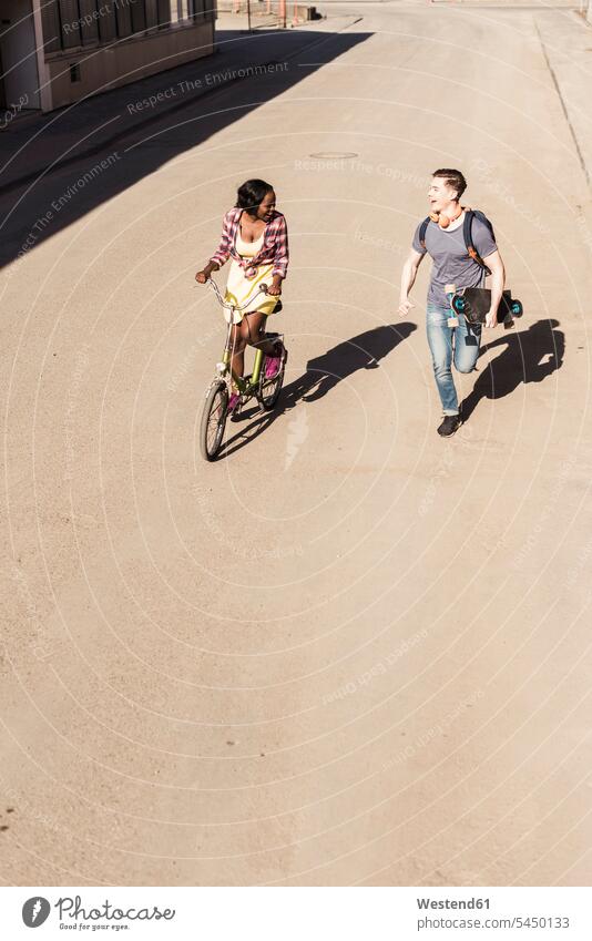 Glückliches Paar beim Laufen und Radfahren auf der Straße radfahren fahrradfahren radeln aktiv fröhlich Fröhlichkeit Frohsinn Heiterkeit jung multikulturell