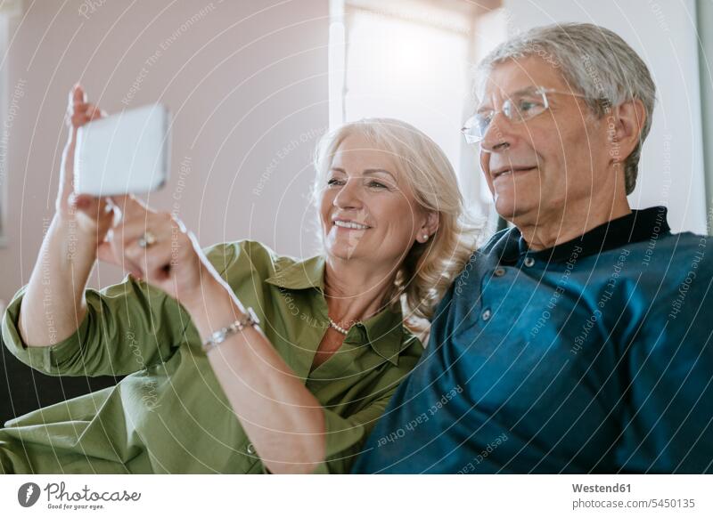 Älteres Paar zu Hause auf der Couch sitzend und ein Selfie machend Handy Mobiltelefon Handies Handys Mobiltelefone Selfies Pärchen Paare Partnerschaft Sofa