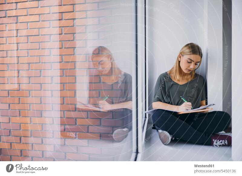Student sitzt am Fenster und lernt auf dem Flur Unterlagen sitzen studieren Studentin Korridor lernen Akademische Bildung Freizeitkleidung Universität College