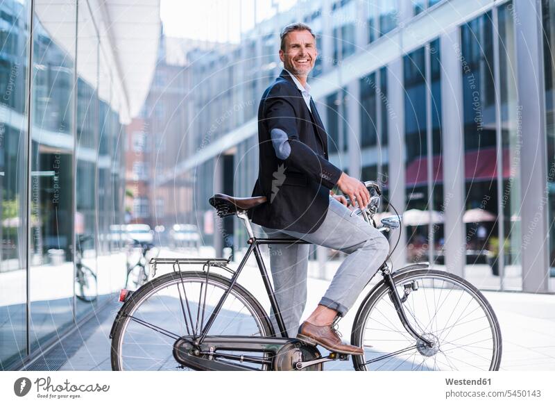 Lächelnder Geschäftsmann auf dem Fahrrad in der Stadt lächeln Bikes Fahrräder Räder Rad Businessmann Businessmänner Geschäftsmänner staedtisch städtisch Raeder