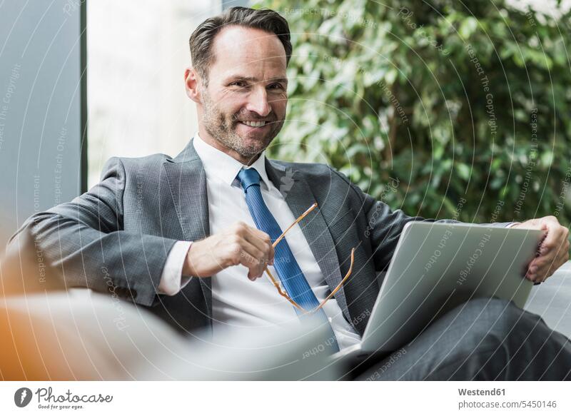 Porträt eines lächelnden Geschäftsmannes in der Lobby mit Laptop Portrait Porträts Portraits Businessmann Businessmänner Geschäftsmänner Geschäftsleute