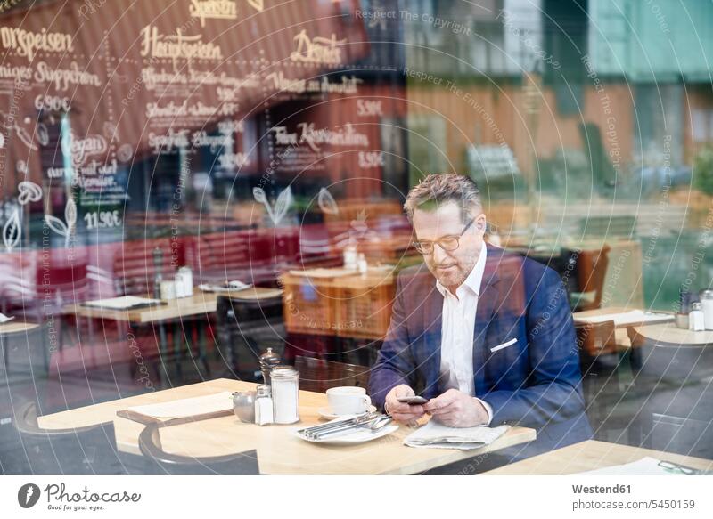 Reifer Geschäftsmann im Cafe mit Handy Businessmann Businessmänner Geschäftsmänner Mobiltelefon Handies Handys Mobiltelefone Kaffeehaus Bistro Cafes Café Cafés