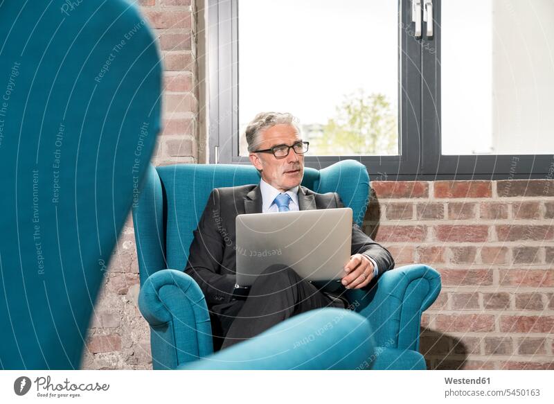 Reifer Geschäftsmann im Sessel sitzend, mit Laptop Notebook Laptops Notebooks sitzt Brille Brillen arbeiten Arbeit Fenster Laptop benutzen Laptop benützen