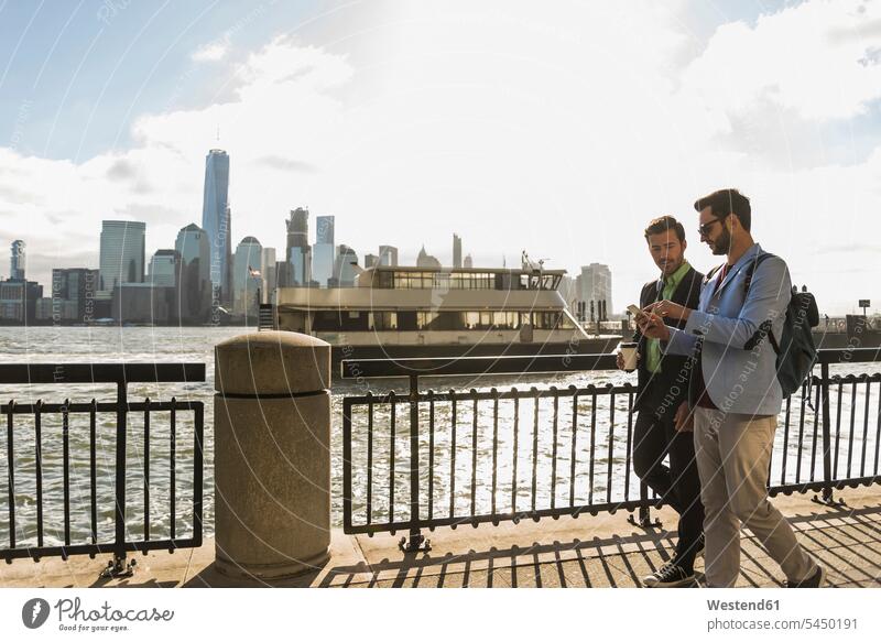 USA, zwei Geschäftsleute zu Fuß am Hafen von New Jersey mit Blick auf Manhattan New York New York State Geschäftsmann Businessmann Businessmänner