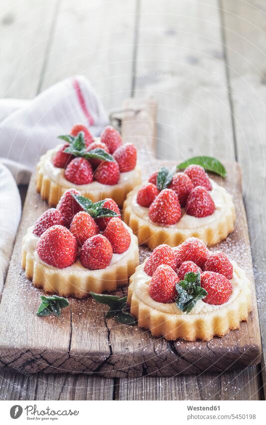 Törtchen mit Puddingfüllung und Erdbeeren süß Süßes Puderzucker angerichtet garniert servierfertig Holzbrett Holzplatten Holzbretter Dessert Nachspeise Desserts