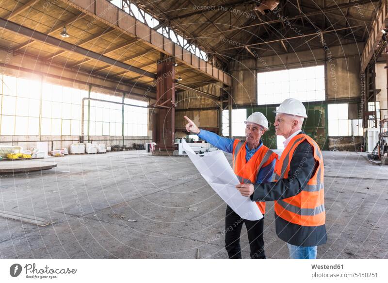 Zwei Männer mit Plan in Sicherheitswesten unterhalten sich in alter Industriehalle Bauplan Architekturplan Bauzeichnung Fabrikhalle Industriehallen Fabrikhallen