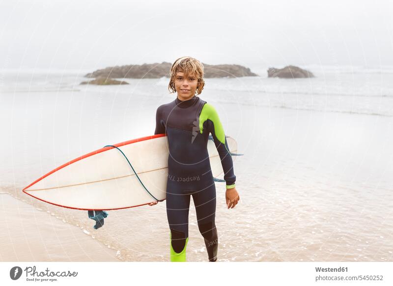 Spanien, Aviles, junger Surfer mit Surfbrett am Strand lächeln Surfbretter surfboard surfboards Meer Meere Teenager Jugendliche Heranwachsende Pubertierende