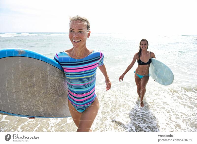 Zwei Frauen im Meer mit Surfbrettern surfboard surfboards lächeln Freundinnen weiblich Surfen Surfing Wellenreiten rennen Wassersport Sport Freunde Freundschaft
