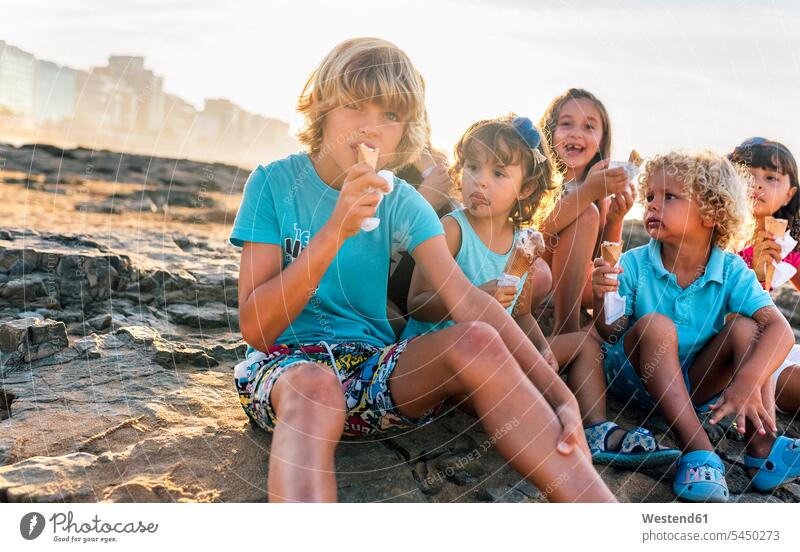 Eine Gruppe von sechs Kindern isst Eiscreme am Strand Speiseeis Kids essen essend Süßspeise Süsses Süßes süß Süßspeisen Essen Food Food and Drink Lebensmittel
