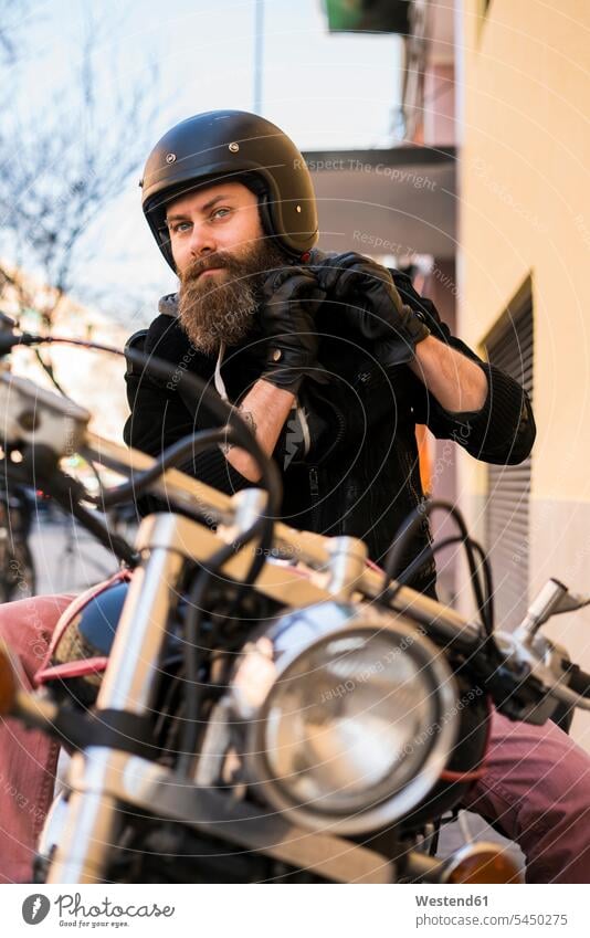 Porträt eines bärtigen Motorradfahrers, der einen Helm befestigt, während er auf seinem Motorrad sitzt Motorräder Kraftfahrzeug Verkehrsmittel KFZ Verkehrswesen